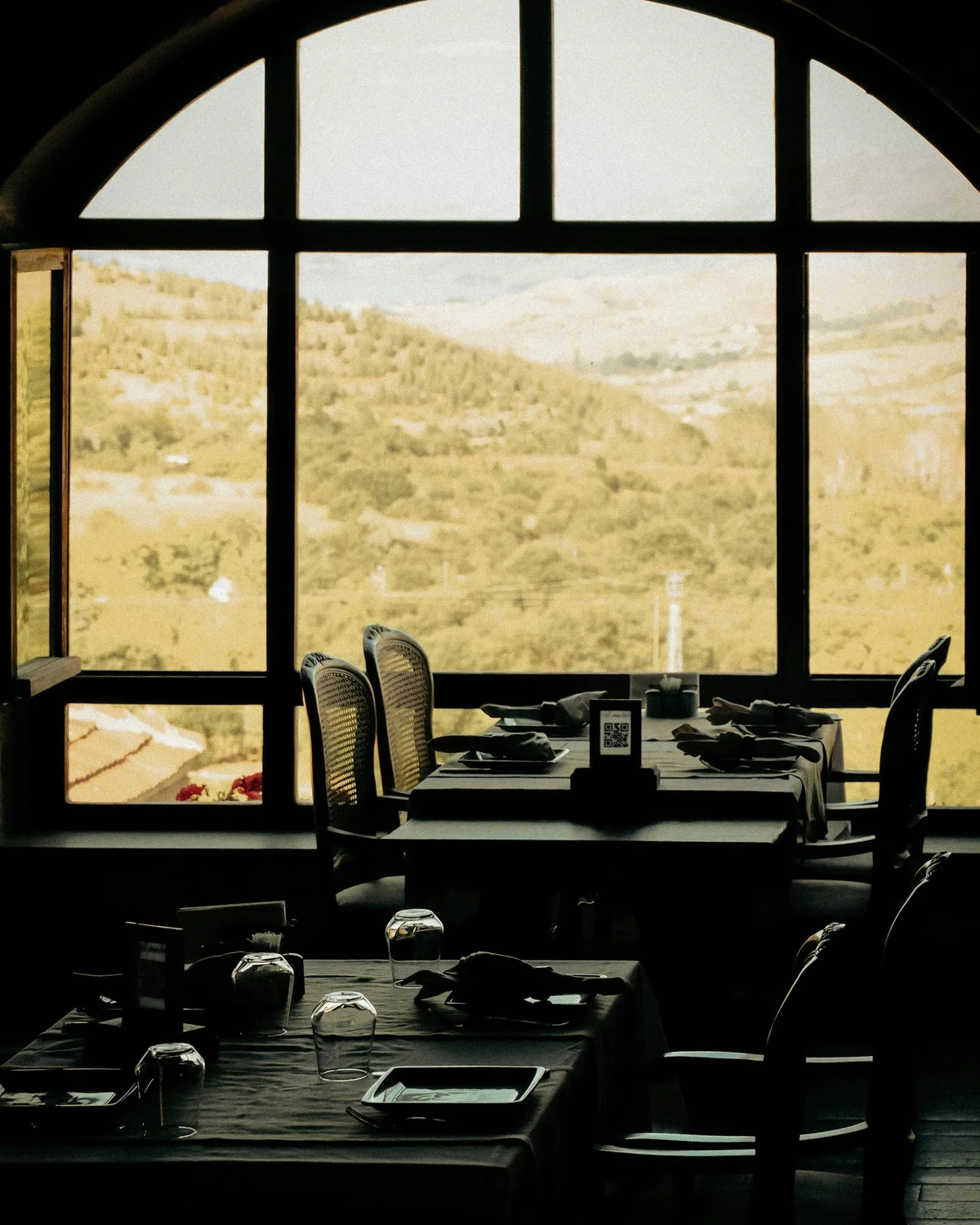 Tables set for a meal beside an arched window overlooking vineyard hills